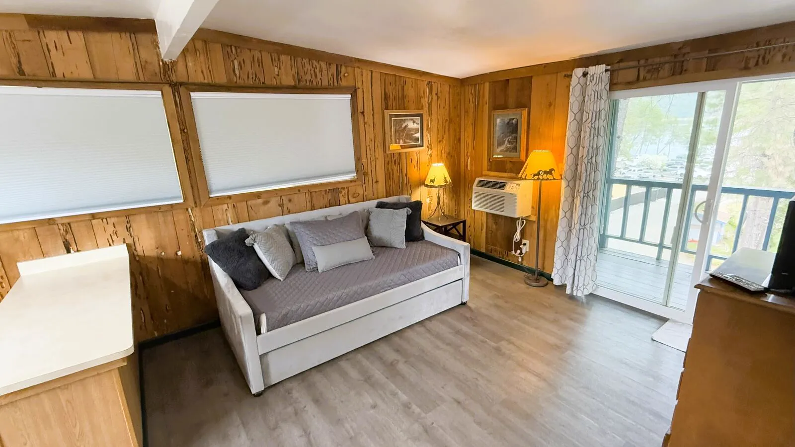Cabin 7 second-deck living room at Silverthorn Resort — daybed with trundle, pine paneling and sliding glass door opening to a private balcony with Shasta Lake and Trinity Forest views