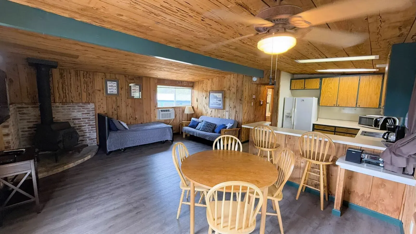 Cabin 8 great room at Silverthorn Resort — wood-burning stove with brick hearth, daybed, futon, dining table and full kitchen in a spacious two-bedroom Shasta Lake family cabin sleeping 8