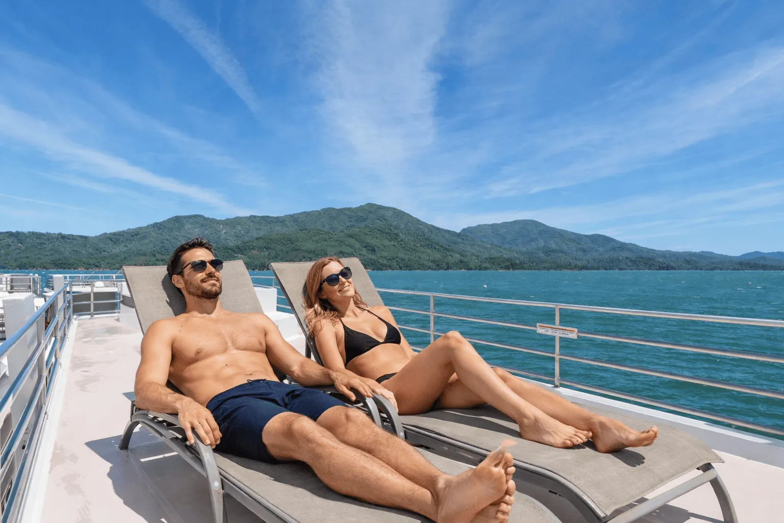 Couple sunbathing on the top deck of a houseboat on Shasta Lake with mountains behind