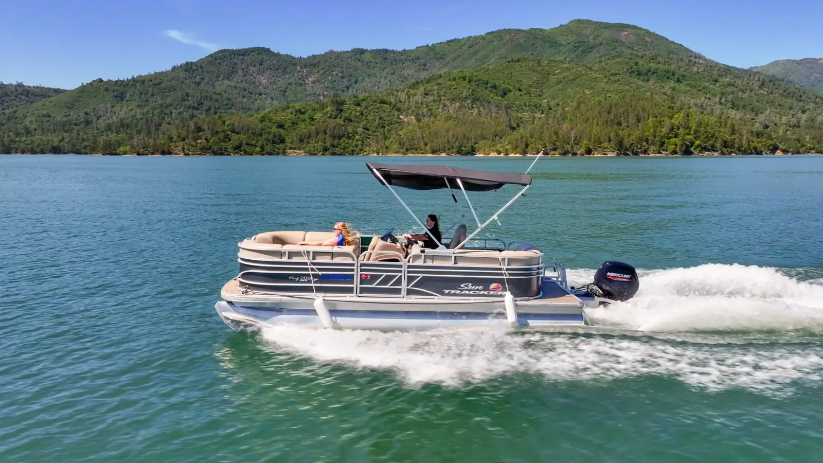 Sun Tracker pontoon boat cruising Shasta Lake with green mountains in the background