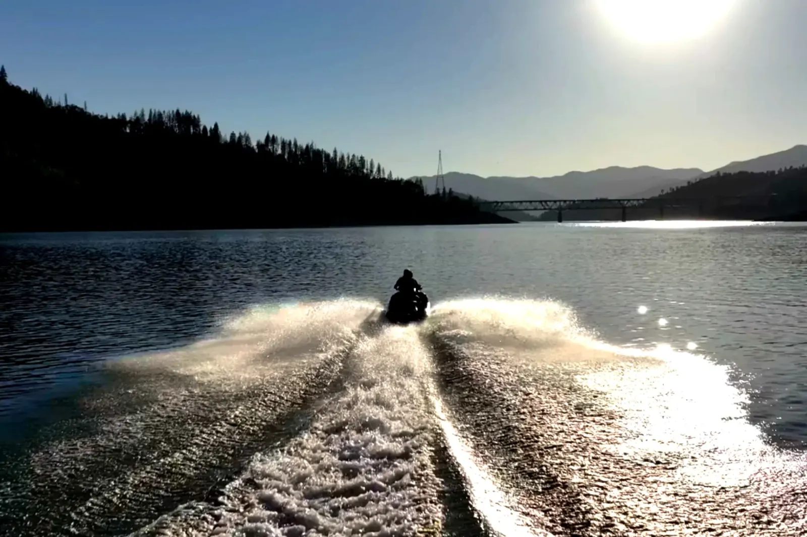 Side view of jet ski riders with the sun setting behind the bridge at Shasta Lake