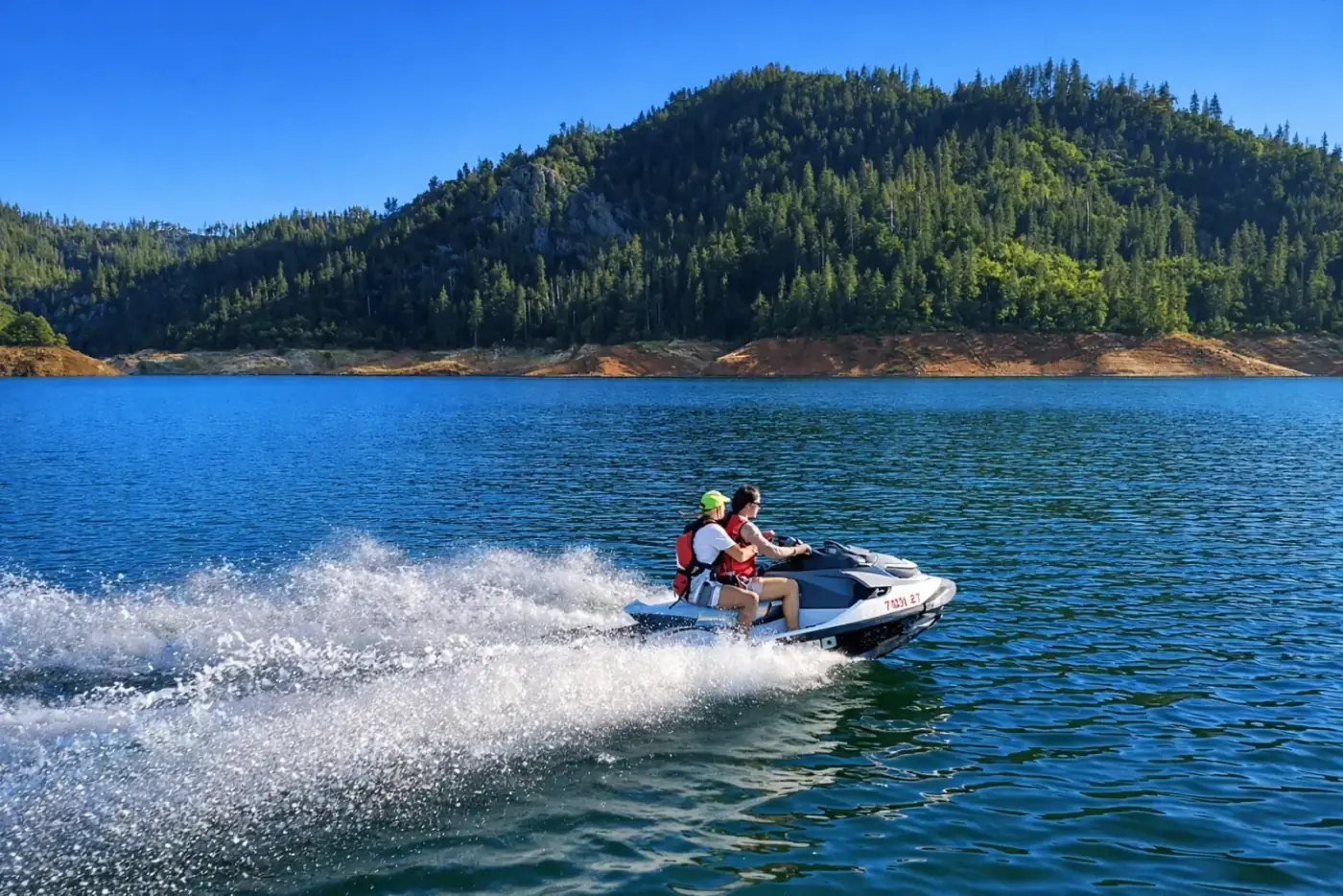 Two riders on a SeaDoo GTX 130 jet ski speeding across Shasta Lake with forested mountains in the background