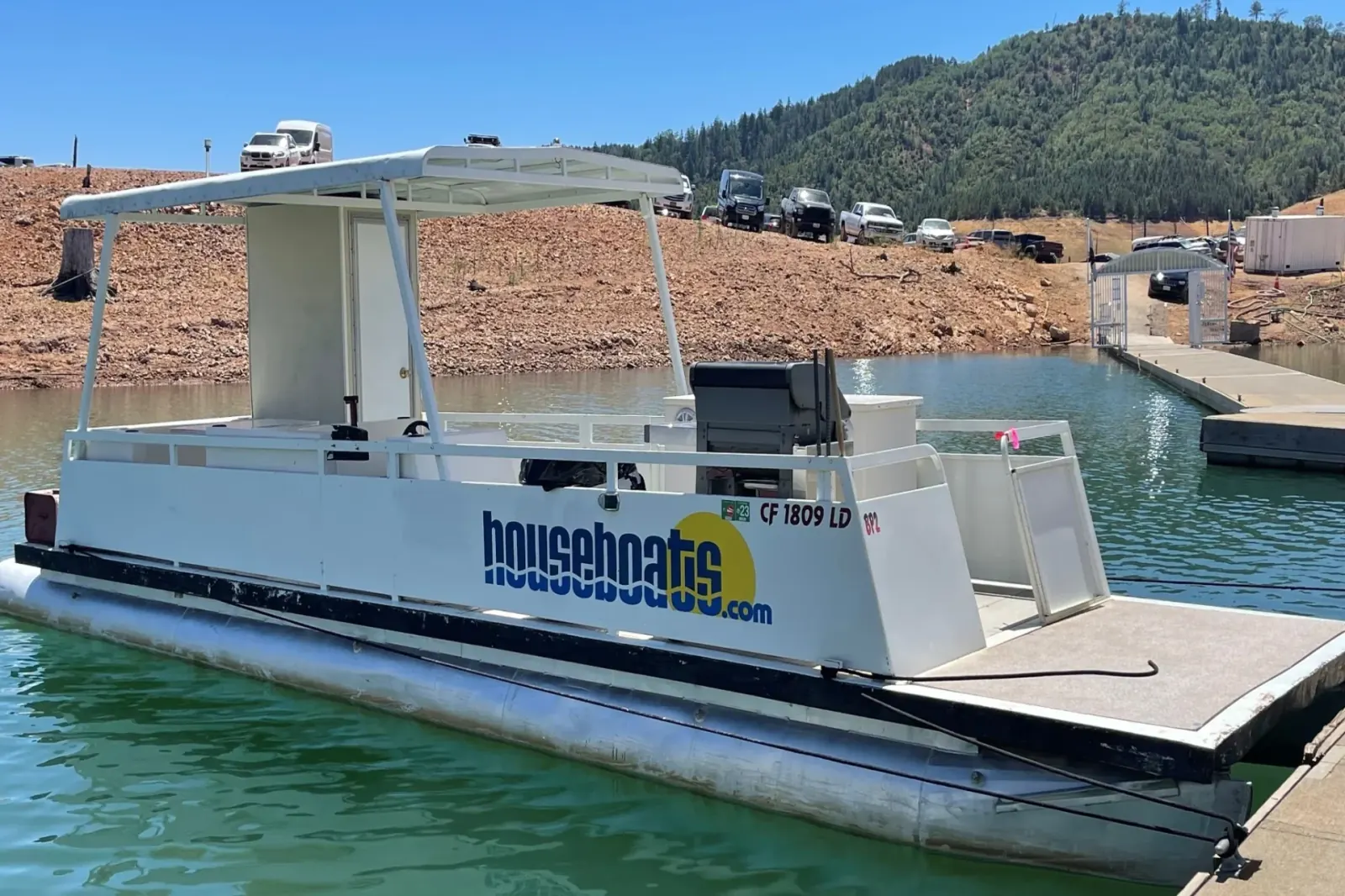 Patio Boat side profile showing flat deck layout docked at Shasta Lake with hillside views