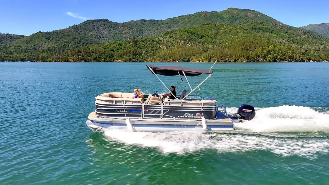 Sun Tracker Pontoon with bimini top cruising past green mountains on Shasta Lake with Mercury outboard