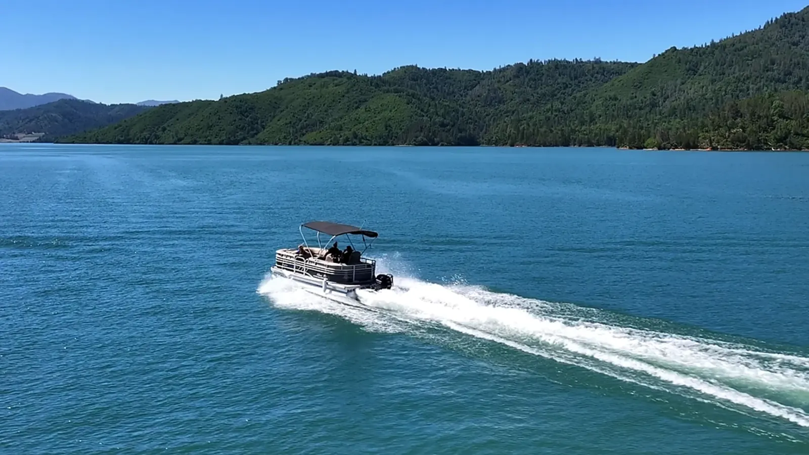 Sun Tracker Pontoon at distance creating wake on Pit River Arm of Shasta Lake with mountain scenery