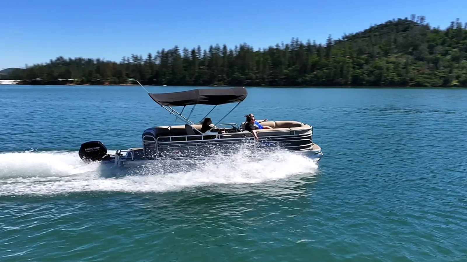 Passengers relaxing on Sun Tracker Pontoon under bimini shade cruising Shasta Lake shoreline