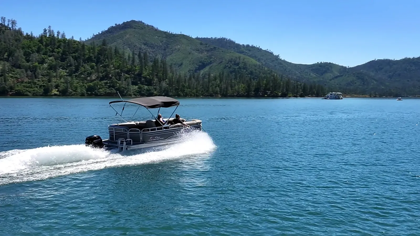 Sun Tracker Pontoon speeding across Shasta Lake with forested mountain backdrop and houseboat in distance